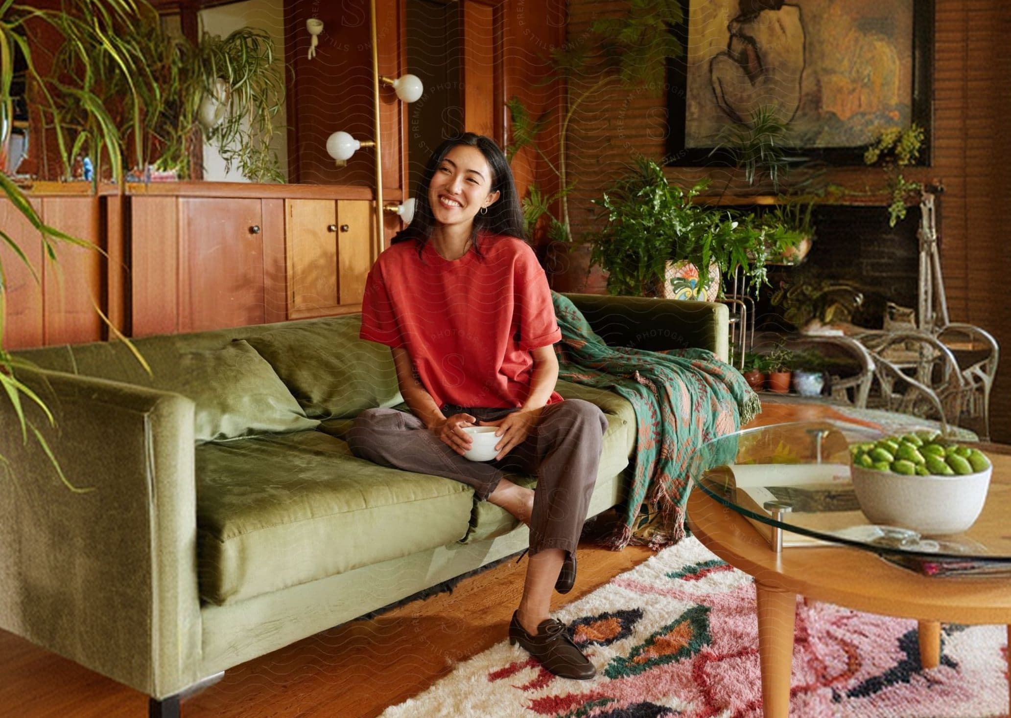A smiling woman sitting on a green sofa holding a bowl
